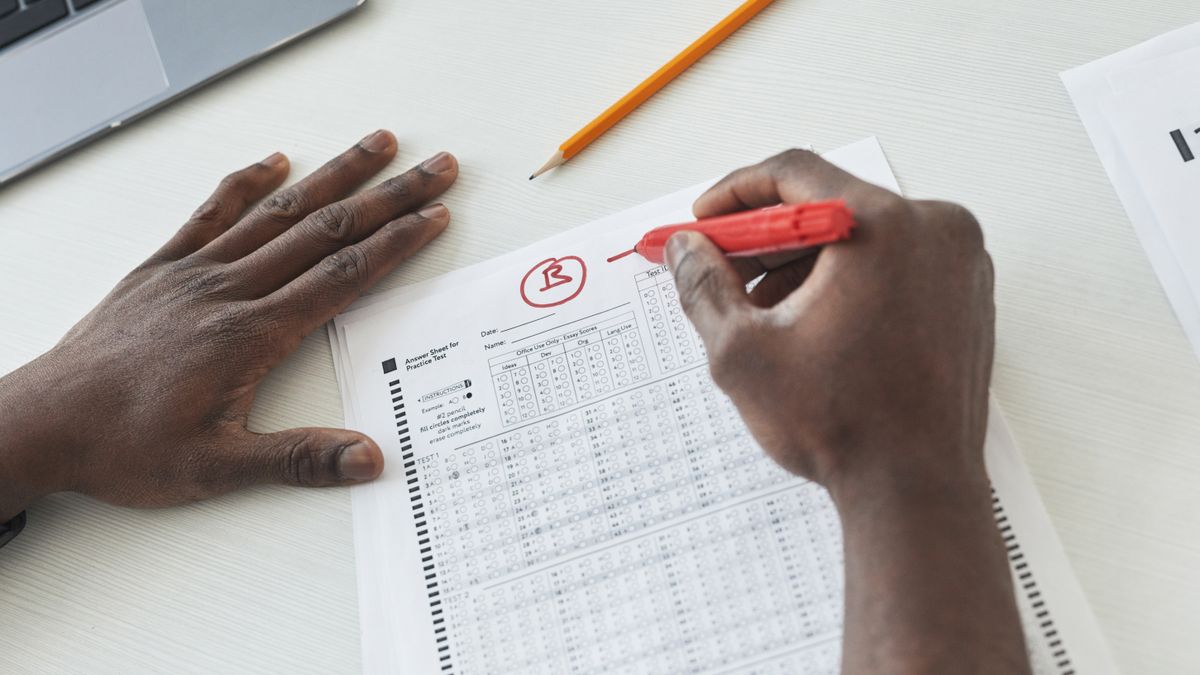 A close-up of a teacher grading a multiple-choice answer sheet with a red pen