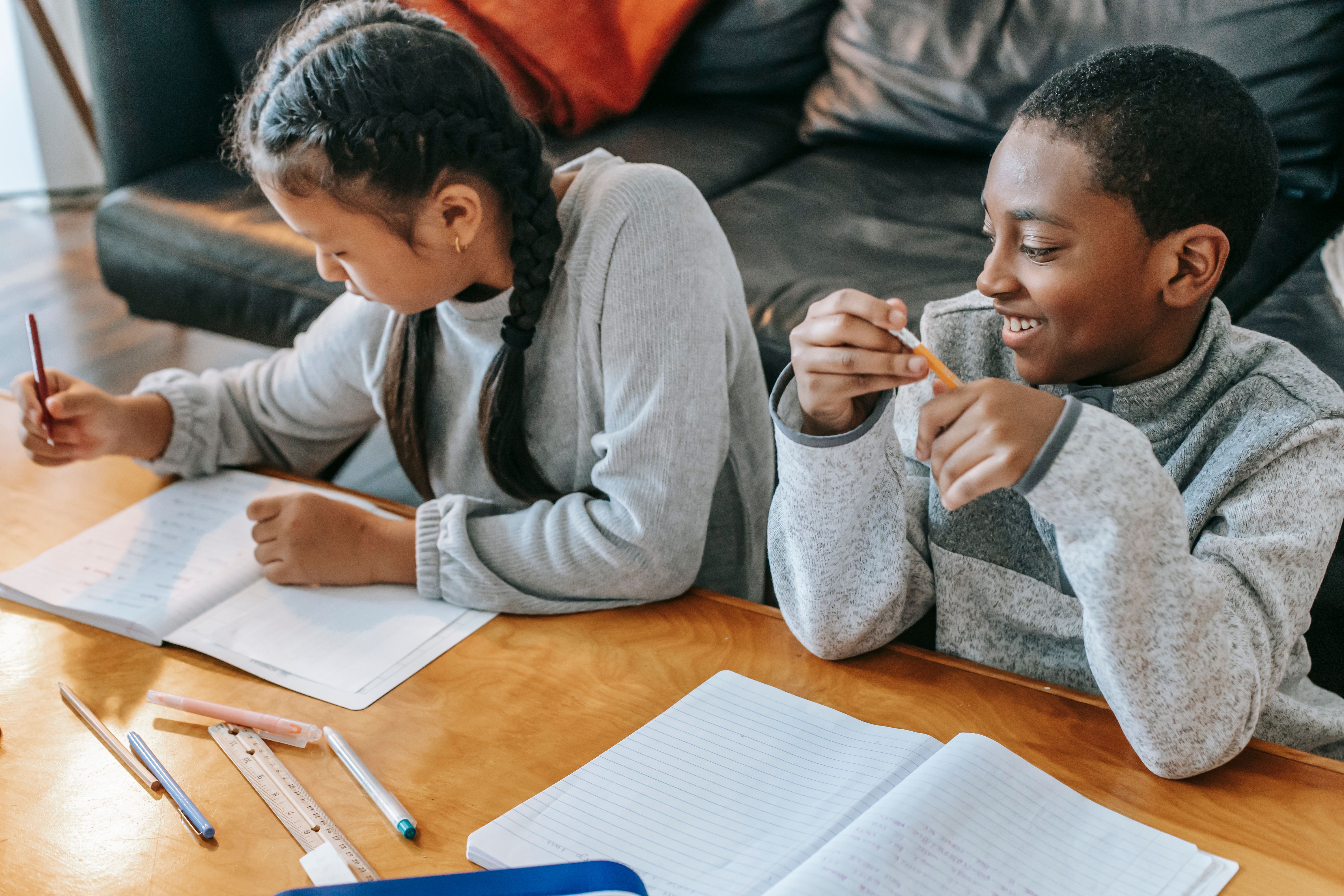 Two children studying together at a table with notebooks and pencils