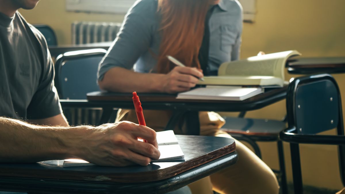 Two students writing notes and working through practice problems at classroom desks