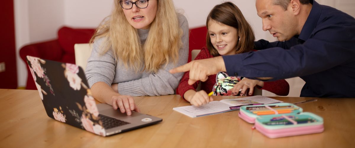 A parent sitting with a child at a laptop during an online class